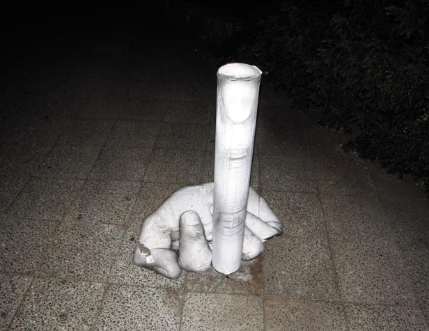 Eine Skulptur einer Hand, die eine Säule hält, steht auf einem gepflasterten Weg.