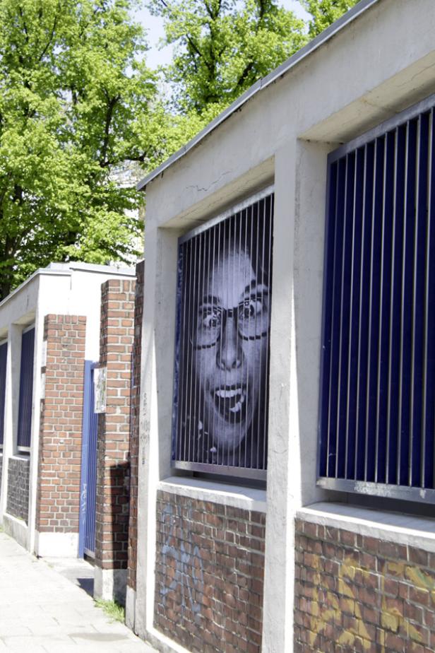Ein Schwarzweiß-Poster einer Frau mit Brille hinter einem vergitterten Fenster.