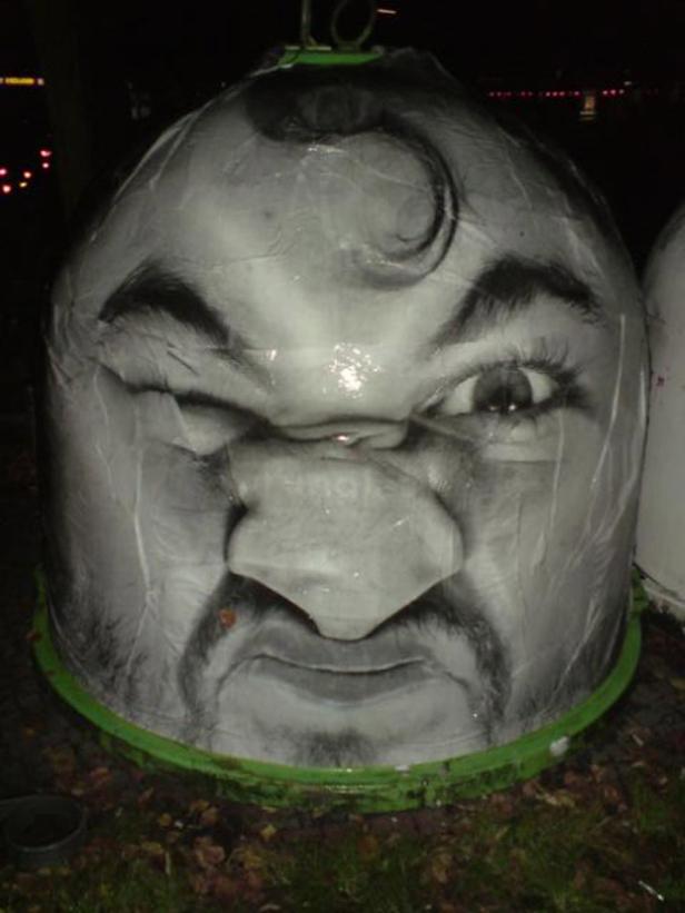 Eine Mülltonne ist mit dem Gesicht eines Mannes mit zusammengekniffenem Auge bemalt.