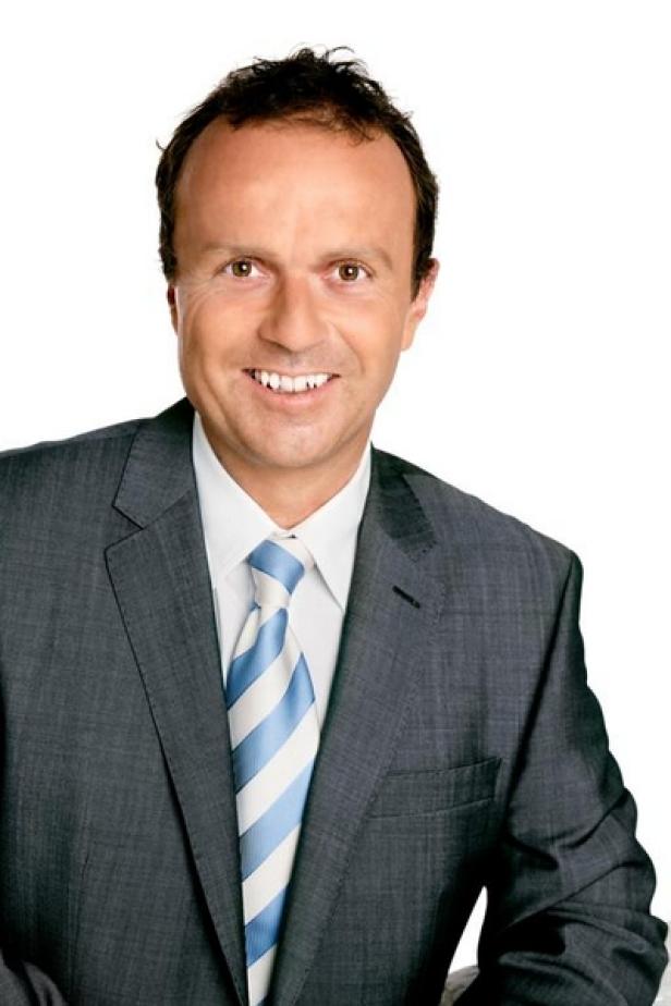 Ein lächelnder Mann im Anzug mit blau-weiß gestreifter Krawatte.