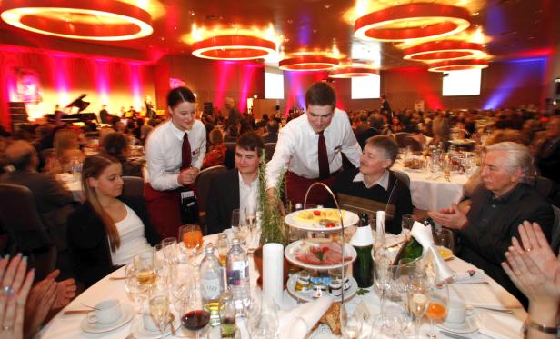 In einem festlichen Saal werden Gäste von Kellnern bedient.
