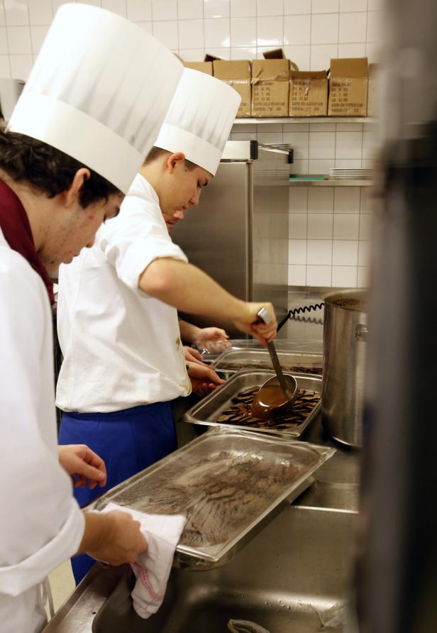 Zwei Köche in Kochmützen arbeiten in einer Küche an Schokoladendesserts.