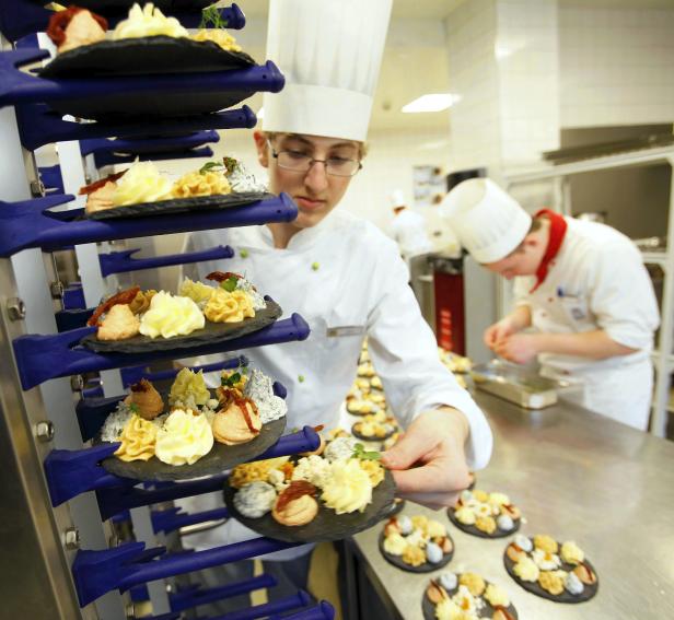 Ein Koch bereitet in einer Küche Canapés auf Schieferplatten vor.