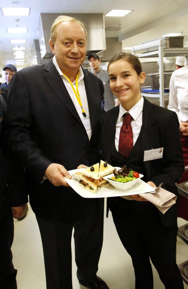 Ein Mann und eine junge Frau präsentieren Sandwiches und Salat in einer Küche.