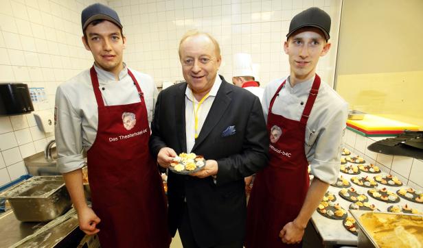 Ein Mann in Anzug hält einen Teller mit Appetithäppchen zwischen zwei Köchen des Theaterhotel-b4C.