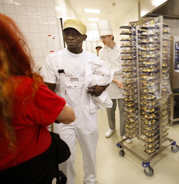 Ein Koch in weißer Arbeitskleidung steht in einer Küche neben einem Wagen mit Appetithäppchen.