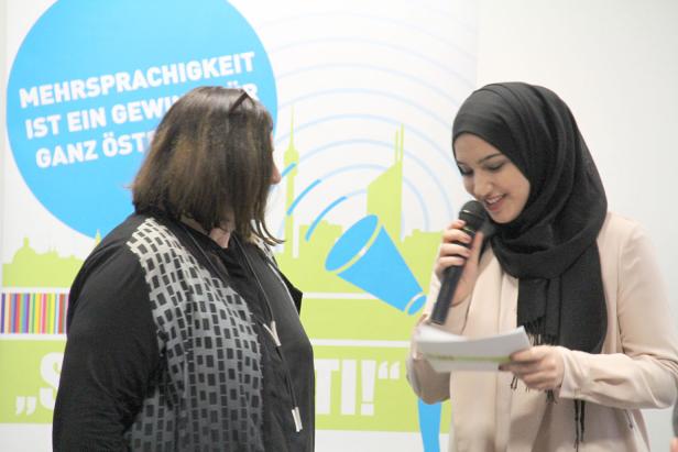 Eine junge Frau mit Hijab spricht bei einer Veranstaltung ins Mikrofon.