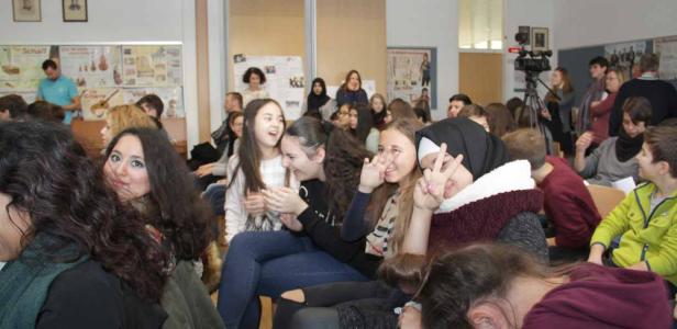Eine Gruppe von Schülerinnen und Schülern sitzt in einem Klassenzimmer und schaut in Richtung einer Kamera.