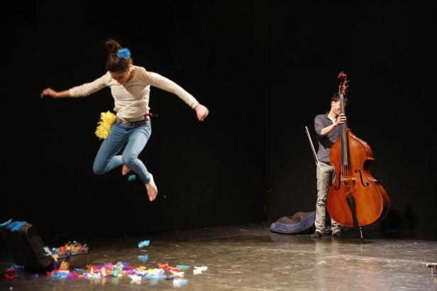 Eine Frau springt barfuß auf einer Bühne, während ein Mann einen Kontrabass hält.