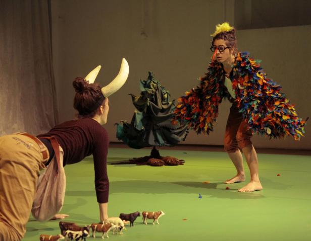 Eine Frau mit Hörnern und eine andere mit Federn stehen auf einer Bühne mit Spielzeugtieren.