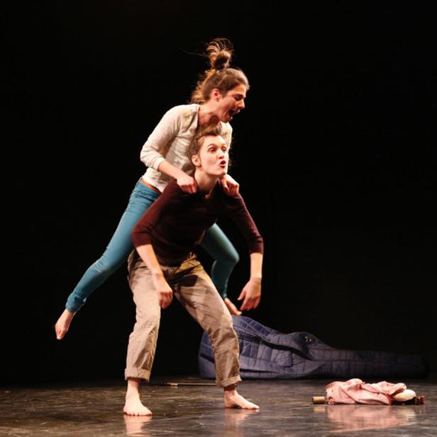 Zwei barfüßige Frauen führen eine Theatervorstellung auf einer Bühne auf.