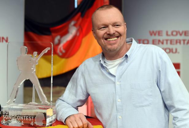 Ein lächelnder Mann steht neben einer Trophäe des Bundesvision Songcontests 2014.