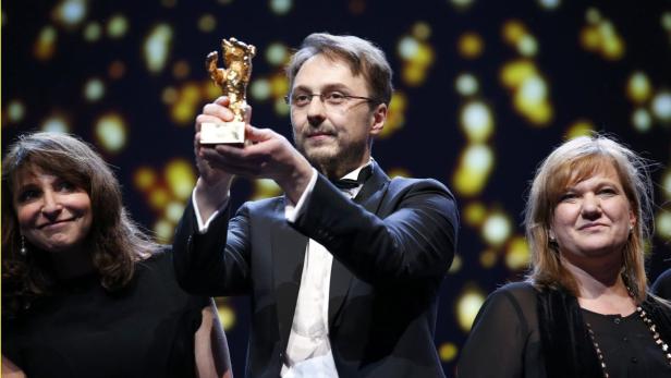 Ein Mann im Anzug hält eine goldene Bärenstatue in die Höhe.