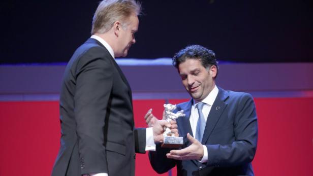 Ein Mann überreicht einem anderen eine silberne Bären-Trophäe.