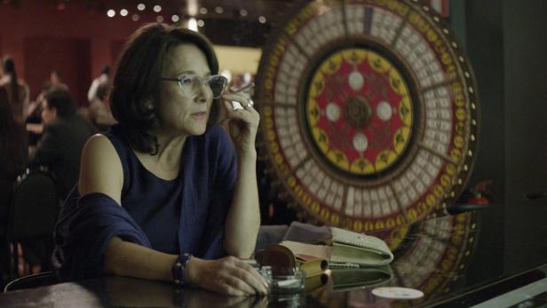 Eine Frau mit Brille raucht in einem Casino eine Zigarette.