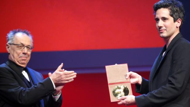 Ein Mann überreicht einem anderen eine goldene Auszeichnung in einer roten Schatulle.