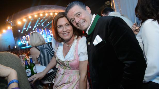 Ein Mann und eine Frau in Tracht posieren vor einer Bühne mit Lichtern.