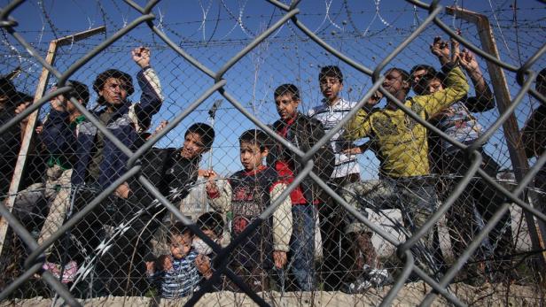 Eine Gruppe von Kindern steht hinter einem Zaun mit Stacheldraht.