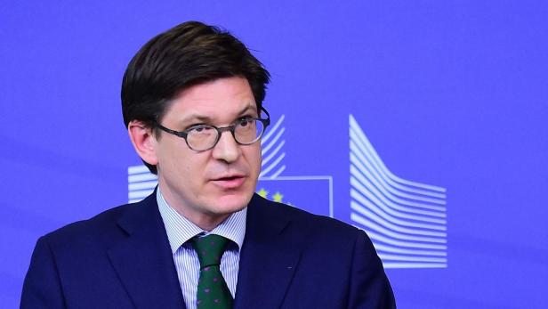 Ein Mann mit Brille und Anzug spricht vor einem blauen Hintergrund mit EU-Logo.