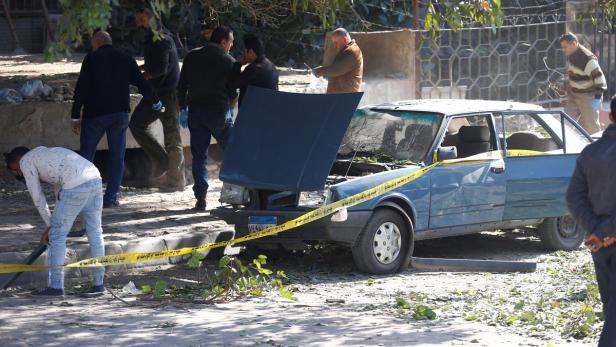 Ein beschädigtes Auto ist mit gelbem Absperrband umgeben, während Personen in der Nähe stehen.