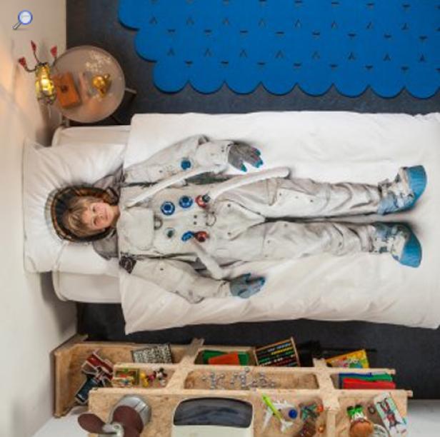 Ein Kind im Astronautenkostüm liegt auf einem Bett.
