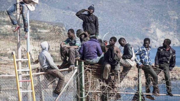 African migrants sit on top of a border fence betw