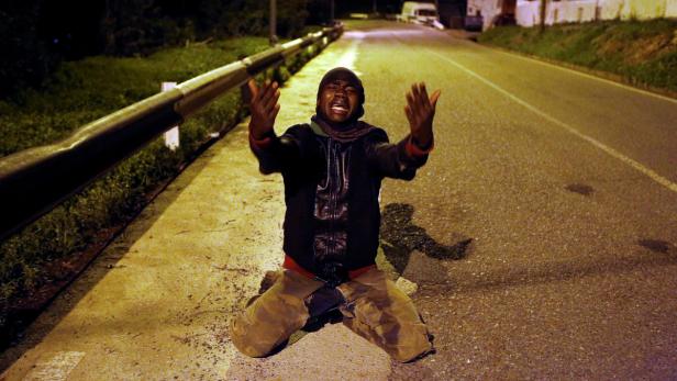 An African migrant reacts on a road after crossing
