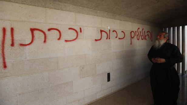 Ein orthodoxer Priester steht vor einer Wand mit hebräischen Graffiti.