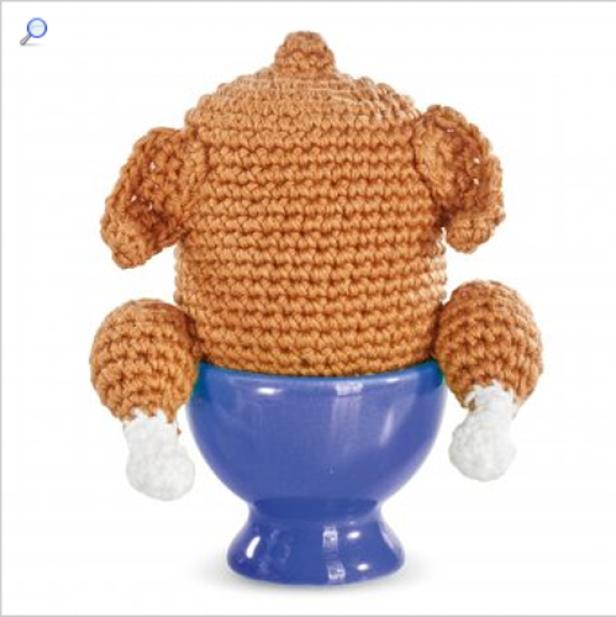 Ein gehäkelter Truthahn sitzt auf einem blauen Eierbecher.