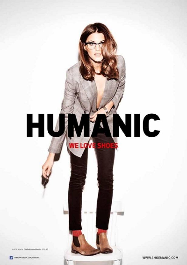 Eine Frau mit Brille, Blazer, Hose und Stiefeletten posiert auf einem Stuhl für eine Humanic-Werbung.