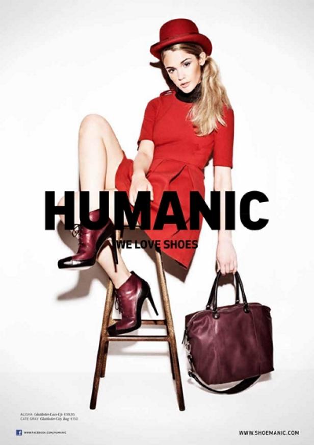 Eine Frau in einem roten Kleid und Hut sitzt auf einem Hocker und präsentiert Schuhe und eine Handtasche von Humanic.