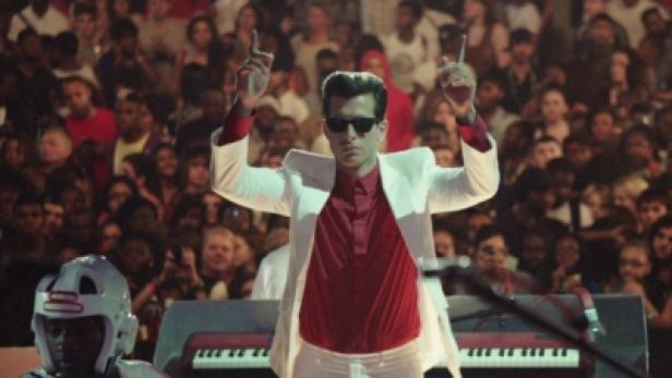 Mark Ronson dirigiert vor einem Publikum mit erhobenen Händen.