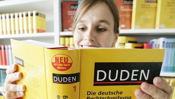 Frau hält einen gelben Duden in der Hand und lächelt dabei.