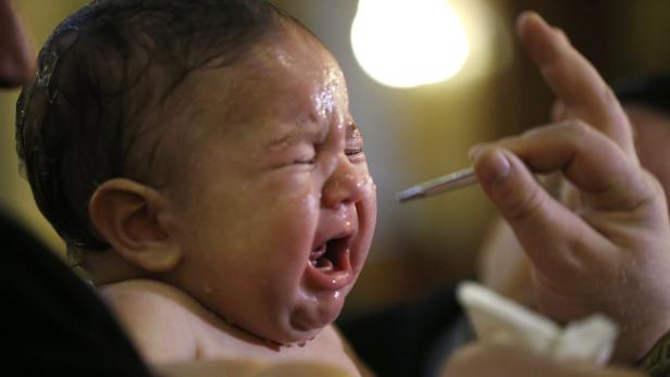 Ein schreiendes Baby wird mit einem Pinsel gesalbt.