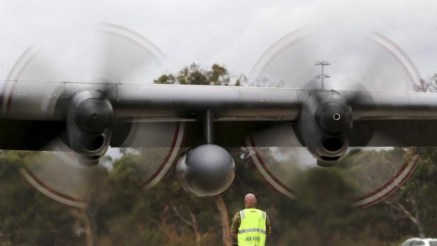 Ein Mann in Sicherheitsweste steht unter den laufenden Propellern eines Flugzeugs.
