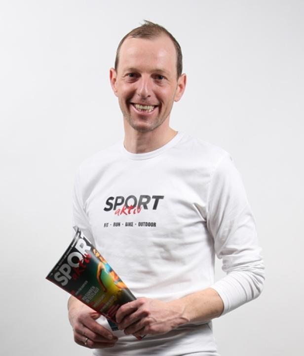 Ein lächelnder Mann im Sport-aktiv-Shirt hält eine Ausgabe des „Sport aktiv“-Magazins.