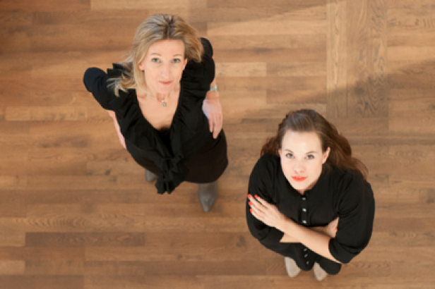 Irene Sagmeister (Herausgeberin), Sarah Posch (Chefredakteurin) - Le Cool Vienna Zwei Frauen in schwarzen Kleidern stehen auf einem Holzboden und schauen nach oben.