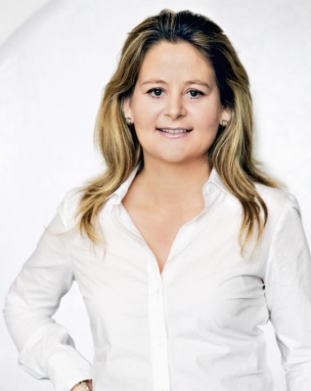 Eine Frau mit blonden Haaren lächelt in einem weißen Hemd.