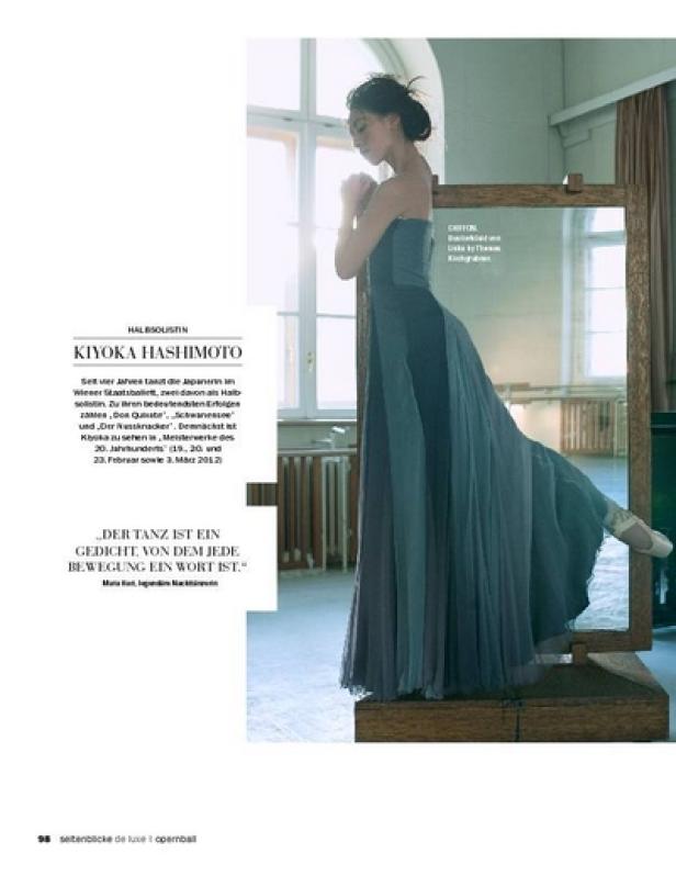 Eine Ballerina in einem langen, fließenden Kleid steht anmutig vor einem Spiegel.