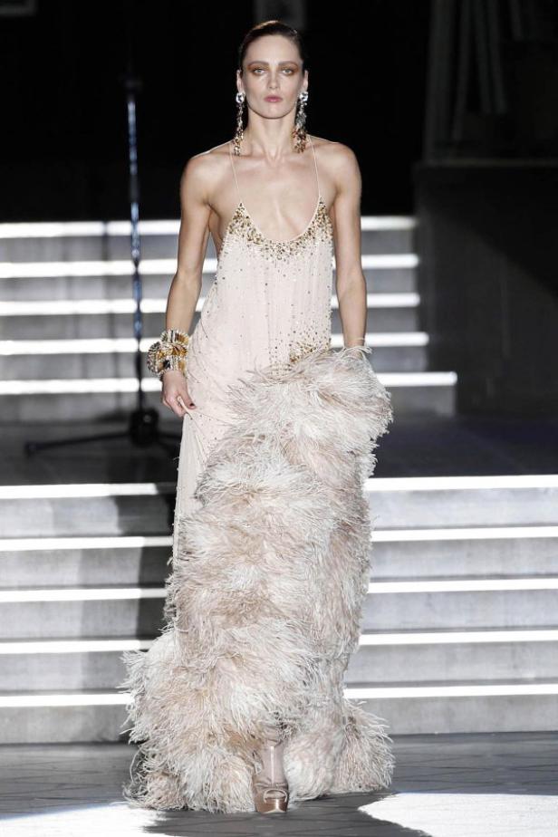 Ein Model präsentiert ein helles, mit Federn besetztes Kleid auf dem Laufsteg.