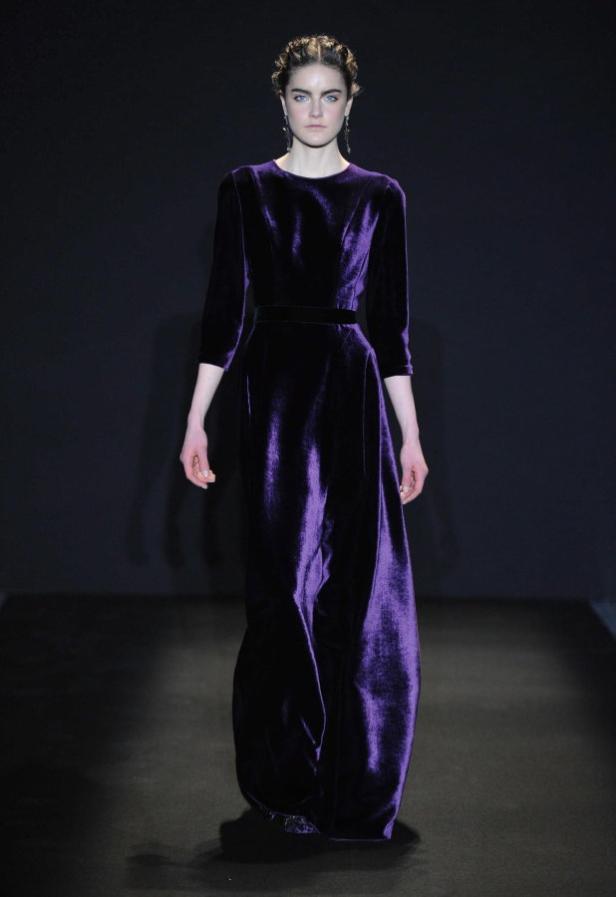 Eine Frau präsentiert ein langes, violettes Samtkleid auf einem Laufsteg.
