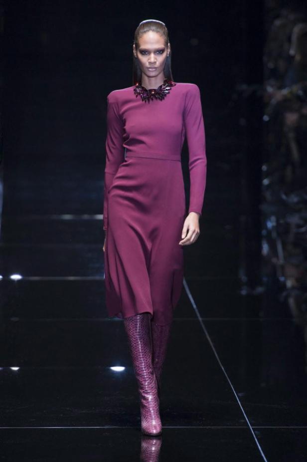 Eine Frau in einem langen, burgunderroten Kleid und passenden Stiefeln auf dem Laufsteg.