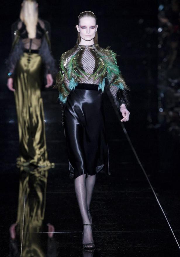 Eine Frau auf dem Laufsteg trägt ein schwarzes Kleid mit Federnbesatz.