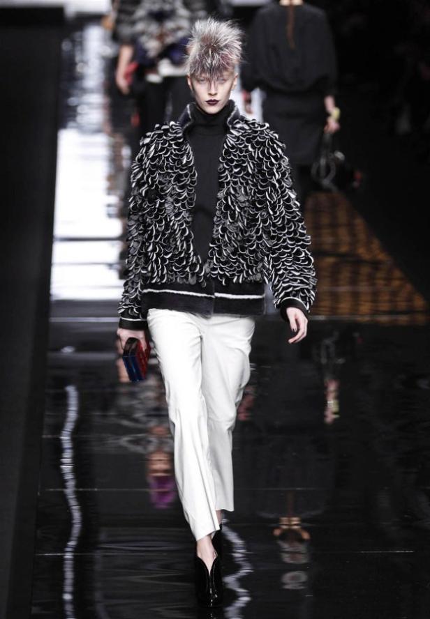 Eine Frau mit extravaganten Haaren läuft auf dem Laufsteg in einer schwarz-weißen Jacke und weißer Hose.