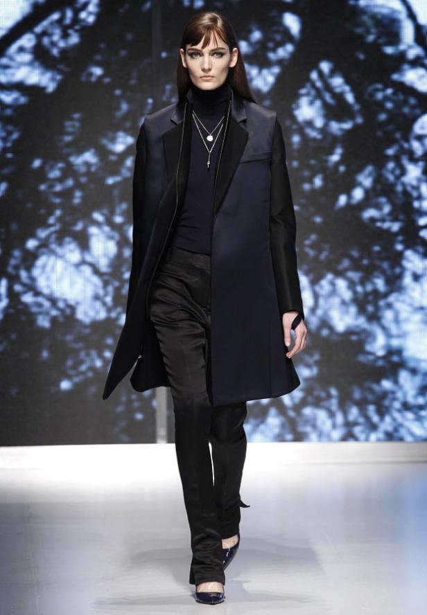 Eine Frau in einem dunklen Mantel und Hose auf einem Laufsteg.