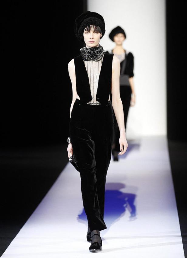 Eine Frau in einem schwarzen Samtanzug und Turban auf einem Laufsteg.