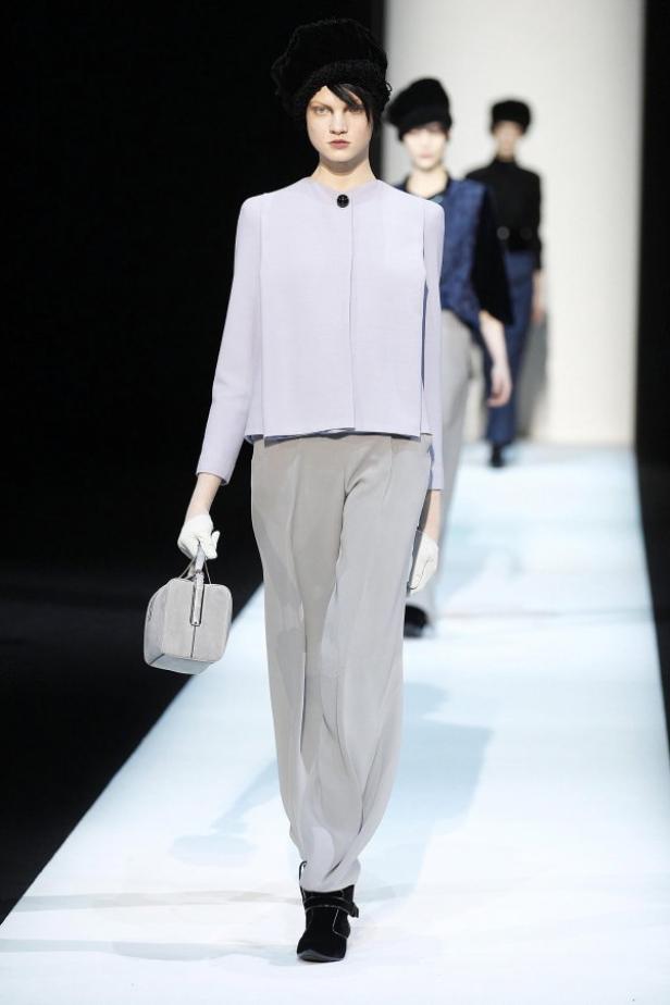 Eine Frau in einem hellblauen Ensemble mit Hut und Handtasche auf dem Laufsteg.