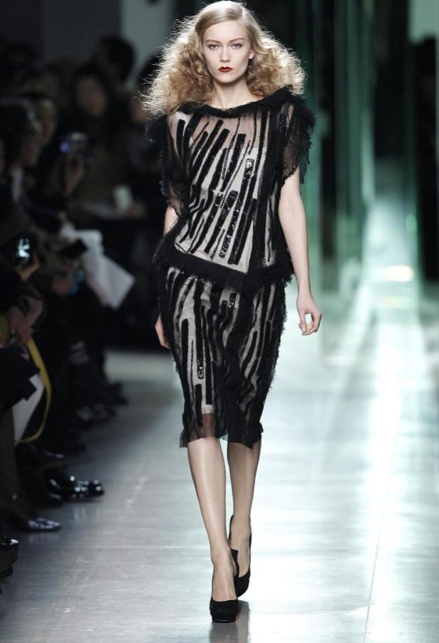 Ein Model präsentiert ein transparentes, schwarz gestreiftes Kleid auf dem Laufsteg.