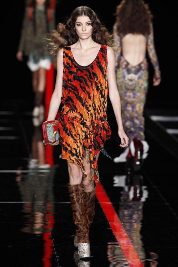 Ein Model mit einem orangefarbenen Kleid mit Tiermuster und passenden Stiefeln auf dem Laufsteg.