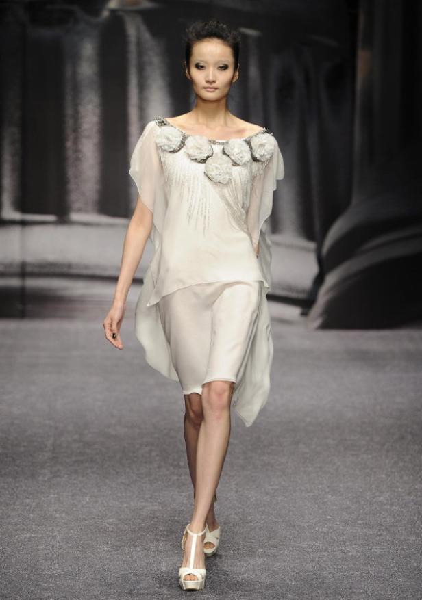 Eine Frau präsentiert ein weißes Kleid mit Blumenapplikationen auf dem Laufsteg.